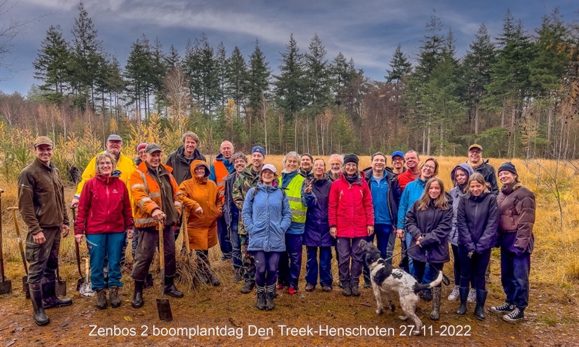 groepsfoto van de boomplantdag, een groep vrijwilligers en een hondje posren lachend voor et et aangeplante perceel